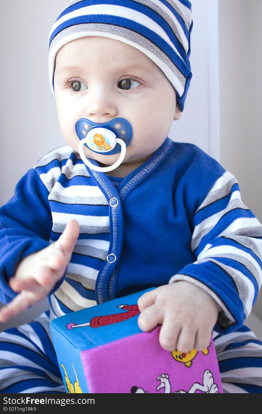 The baby of 6-7 months in a dark blue suit sits with a cube in hands