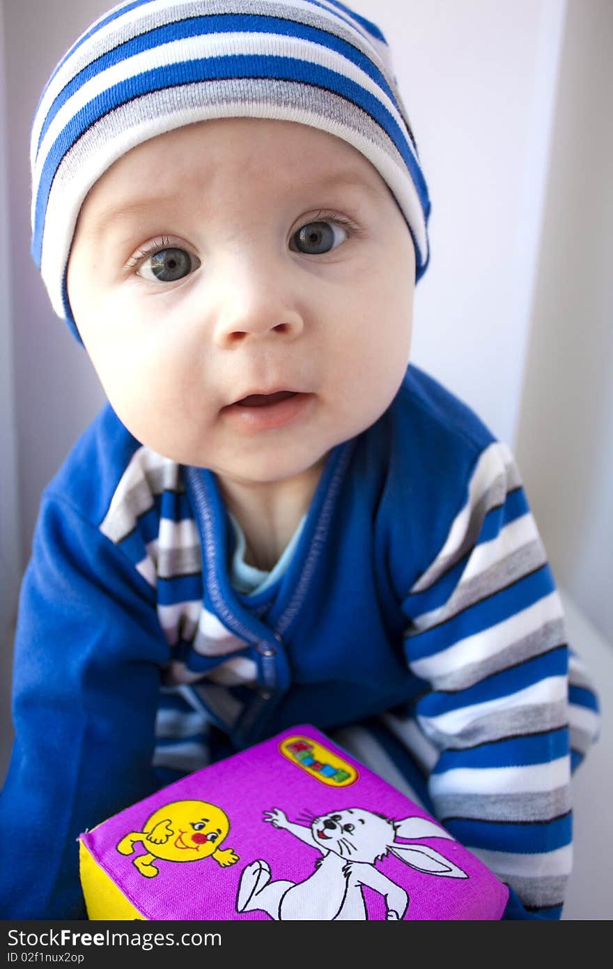 The baby of 6-7 months in a dark blue suit sits with a cube in hands