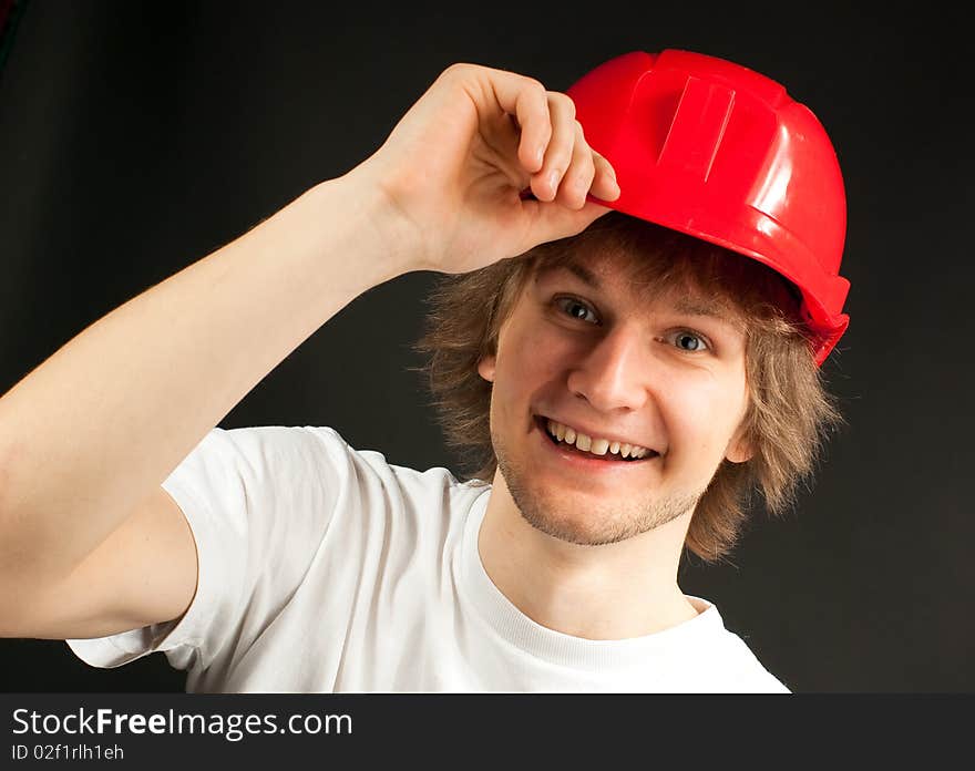 Smiling handsome young man in a red head protector on a dark background. Smiling handsome young man in a red head protector on a dark background