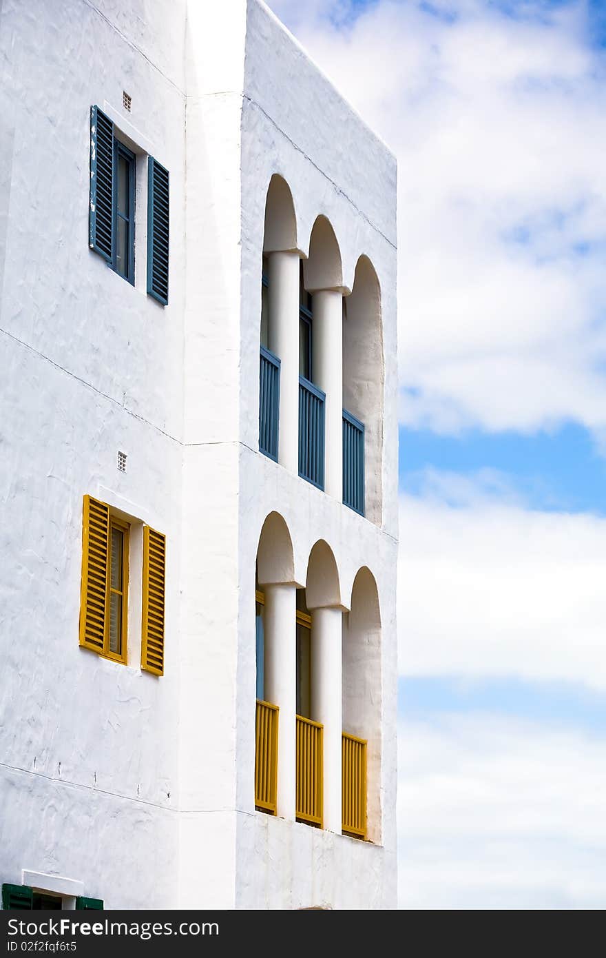 A section of a colourful and vibrant greek styled building with clouds in the background