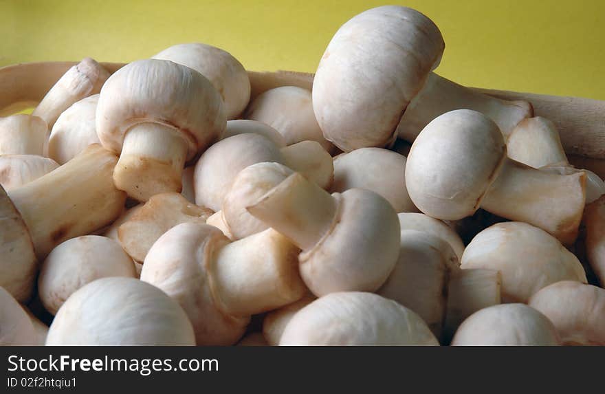 A lot of champignons in a wicker basket on yellow background