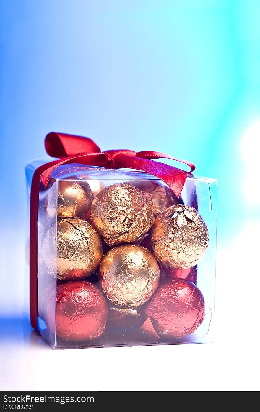 A clear box with gold and red chocolate balls inside it and a red ribbon around it. A clear box with gold and red chocolate balls inside it and a red ribbon around it