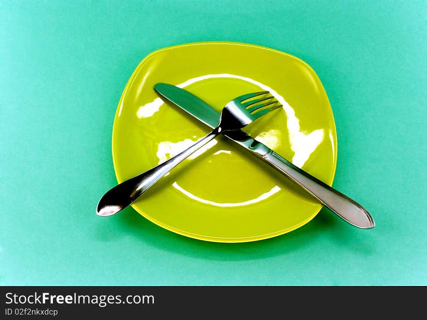 Plate, knife and fork against green background. Plate, knife and fork against green background