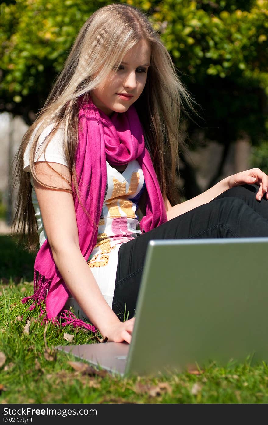 A beautiful attractive blond girl with a laptop in a park. A beautiful attractive blond girl with a laptop in a park