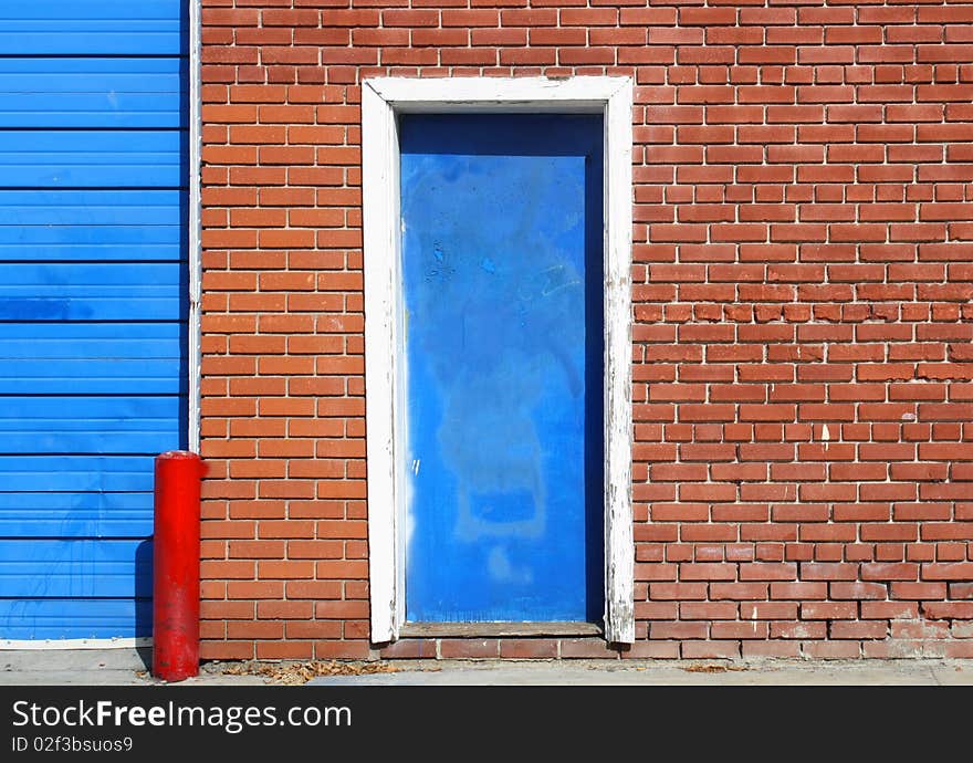 An old blue door in an urban red, brick wall, is seen along a sidewalk. An old blue door in an urban red, brick wall, is seen along a sidewalk.