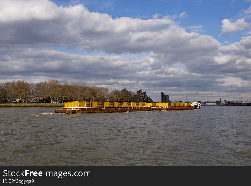 A container barge with cargo on the Thames River in London with beautiful sky. A container barge with cargo on the Thames River in London with beautiful sky