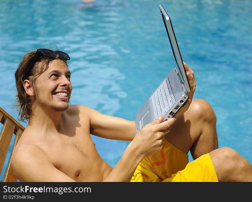 Attractive man uses his laptop while tanning poolside. Attractive man uses his laptop while tanning poolside