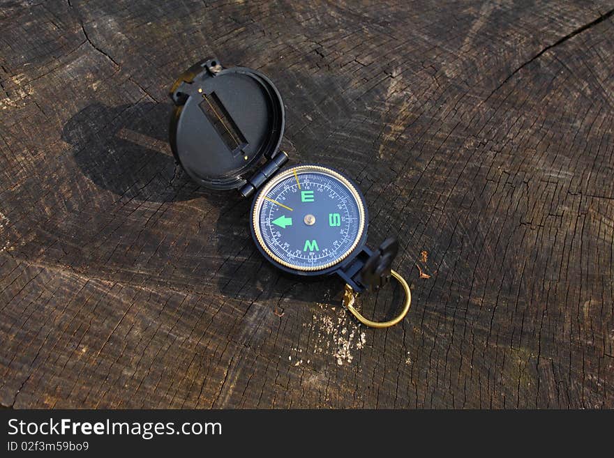 Black and gold plastic compass lying on an old tree stump in the forest. Black and gold plastic compass lying on an old tree stump in the forest