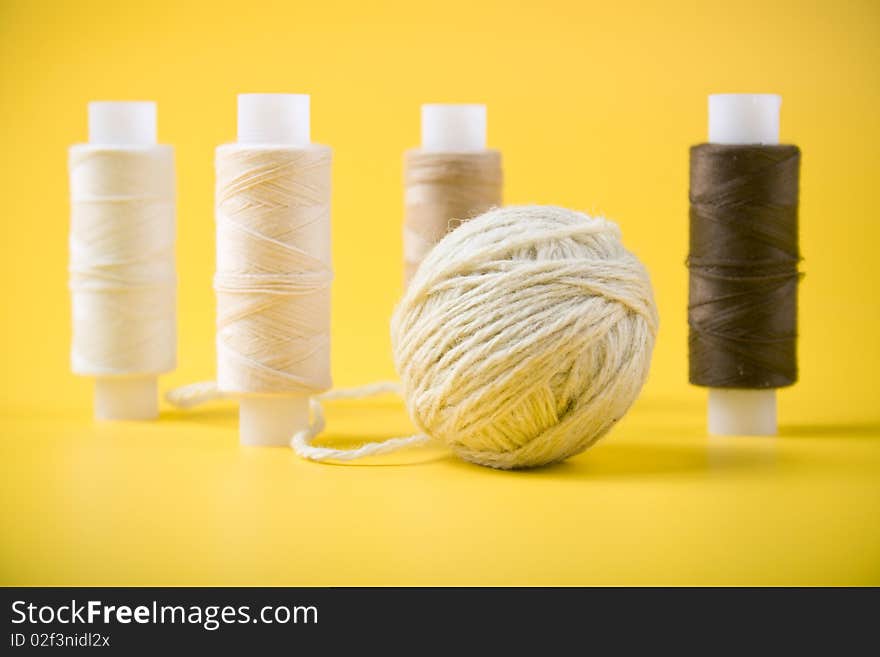 Ball of yarn and spools of thread on a yellow background