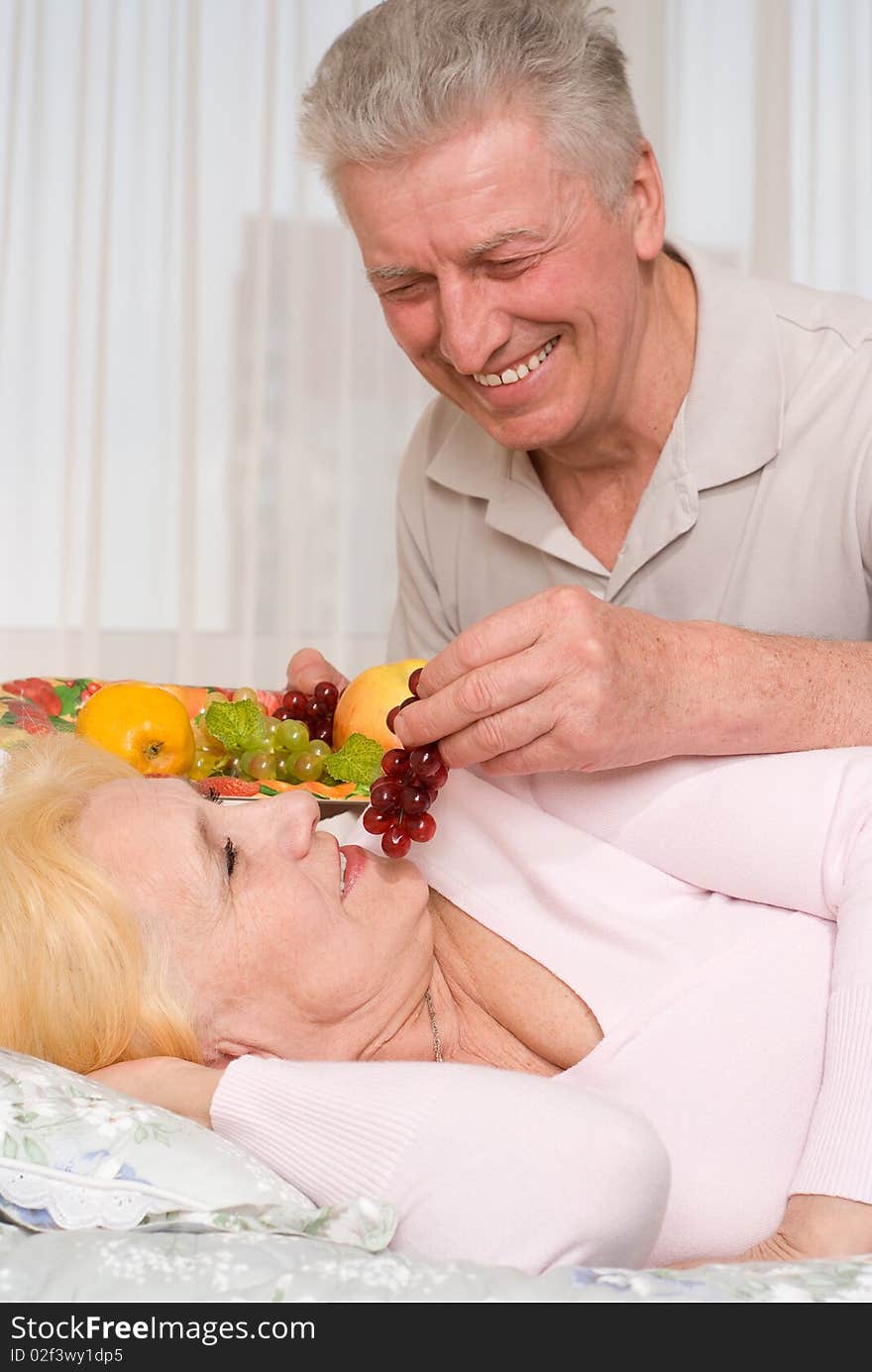 An elderly man brings his wife fruit in bed. An elderly man brings his wife fruit in bed