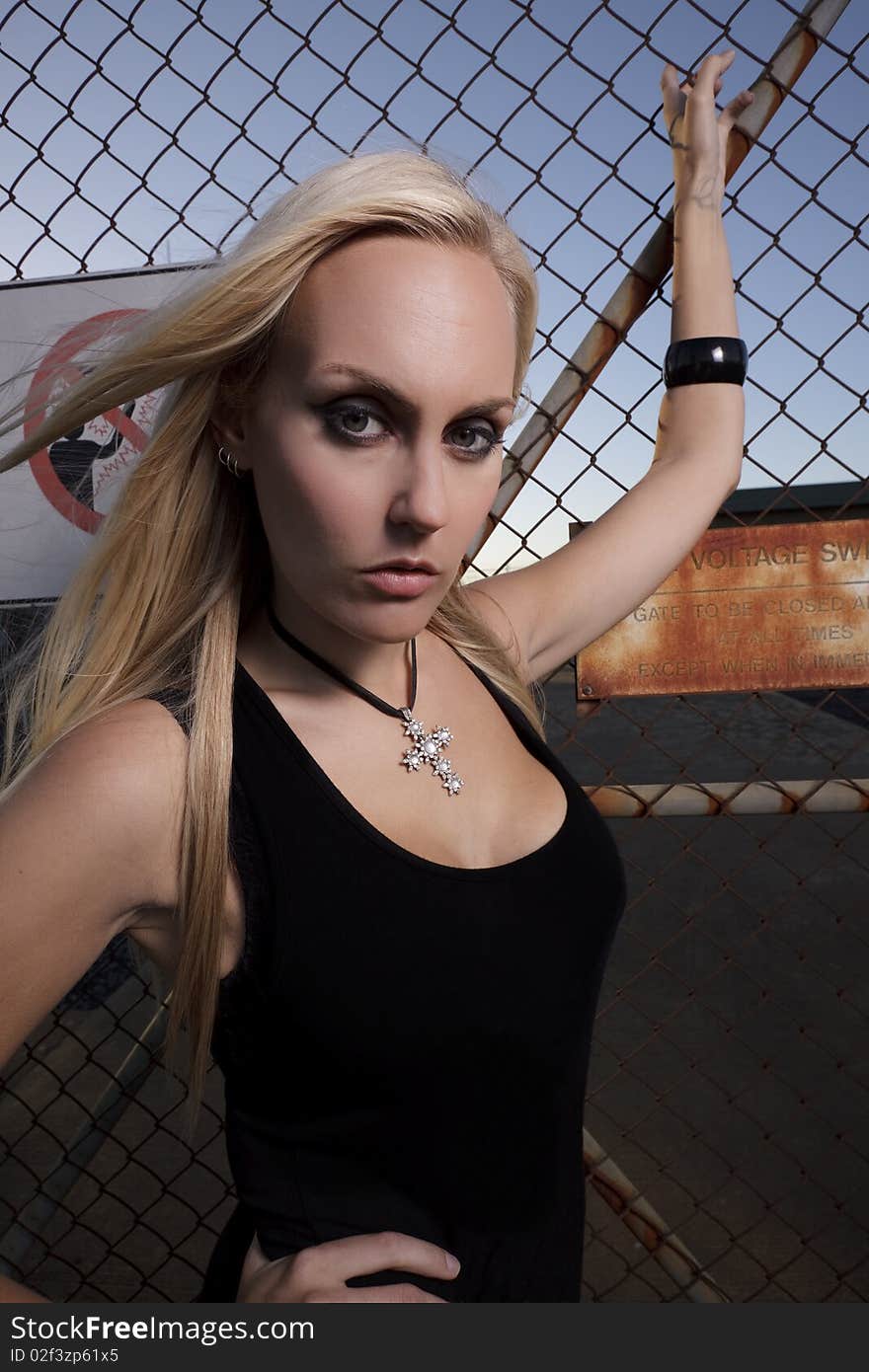 Young female model holding on to a wire fence, next to a danger dign