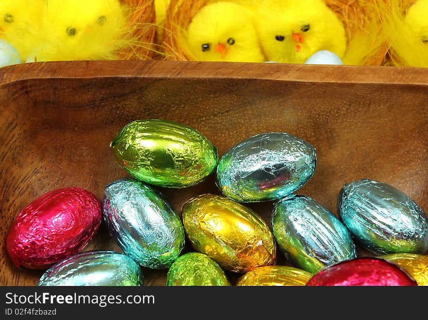 Colorful Chocolate Easter eggs in wooden bowl and yellow chicks in background. Colorful Chocolate Easter eggs in wooden bowl and yellow chicks in background