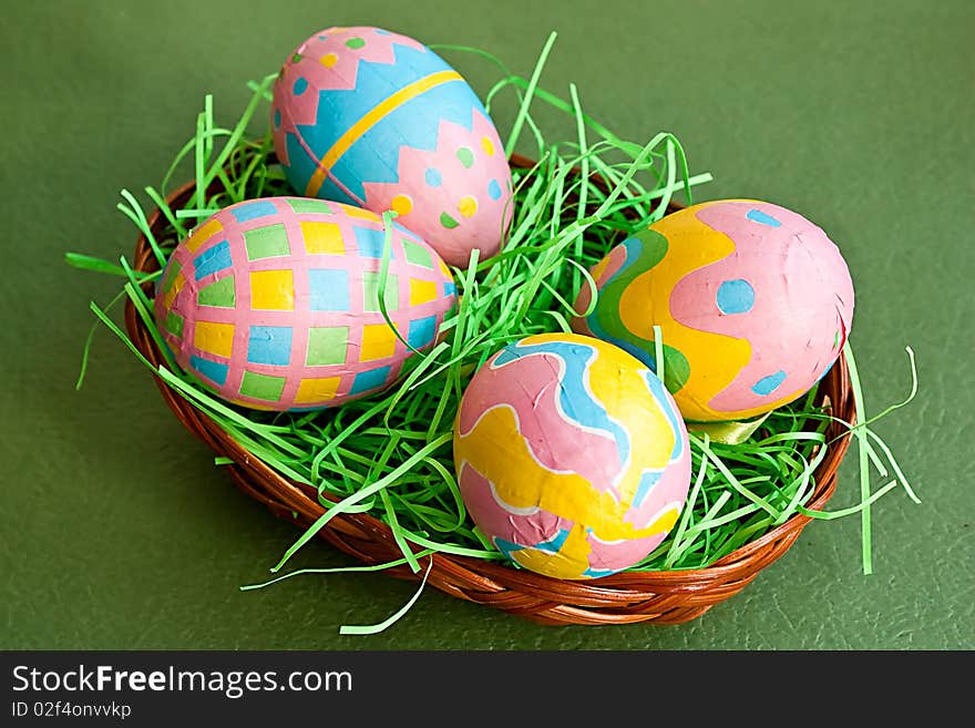 Colored Easter eggs in a basket on green background