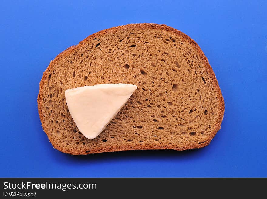 A slice of black bread, cheese and milk in front of blue background. A slice of black bread, cheese and milk in front of blue background