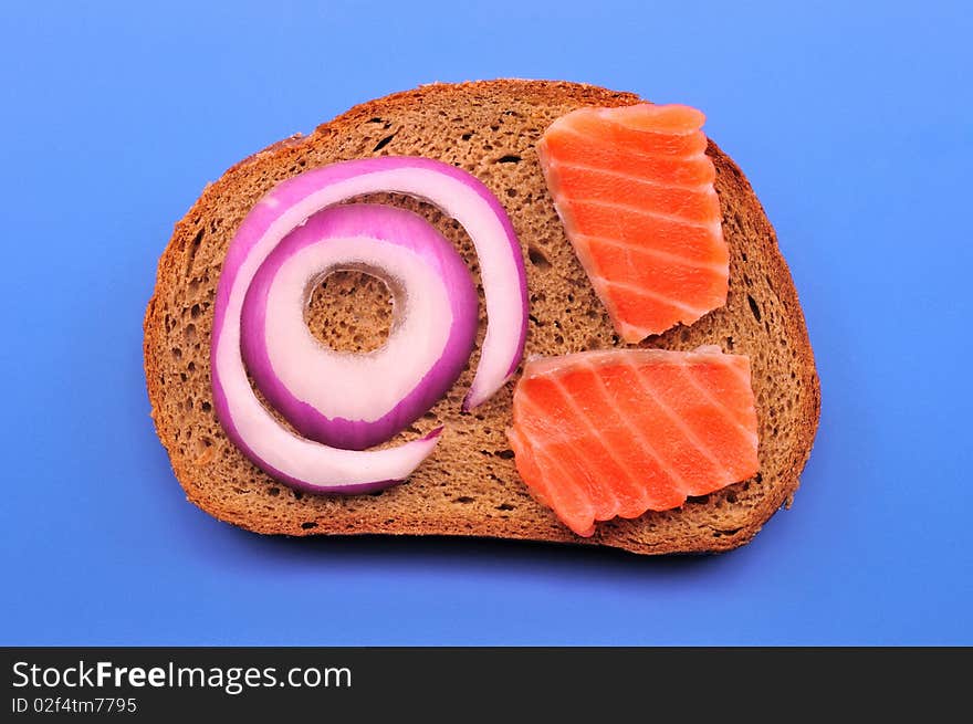 A slice of black bread and two pieces of salmon and onion rings and blue on blue. A slice of black bread and two pieces of salmon and onion rings and blue on blue