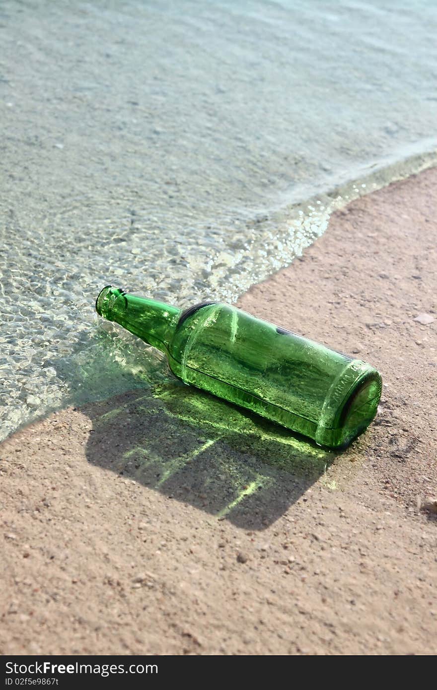 Green glass bottle in a sea wave