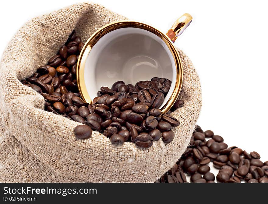 The cup lies in a sack with coffee grains is isolated on white