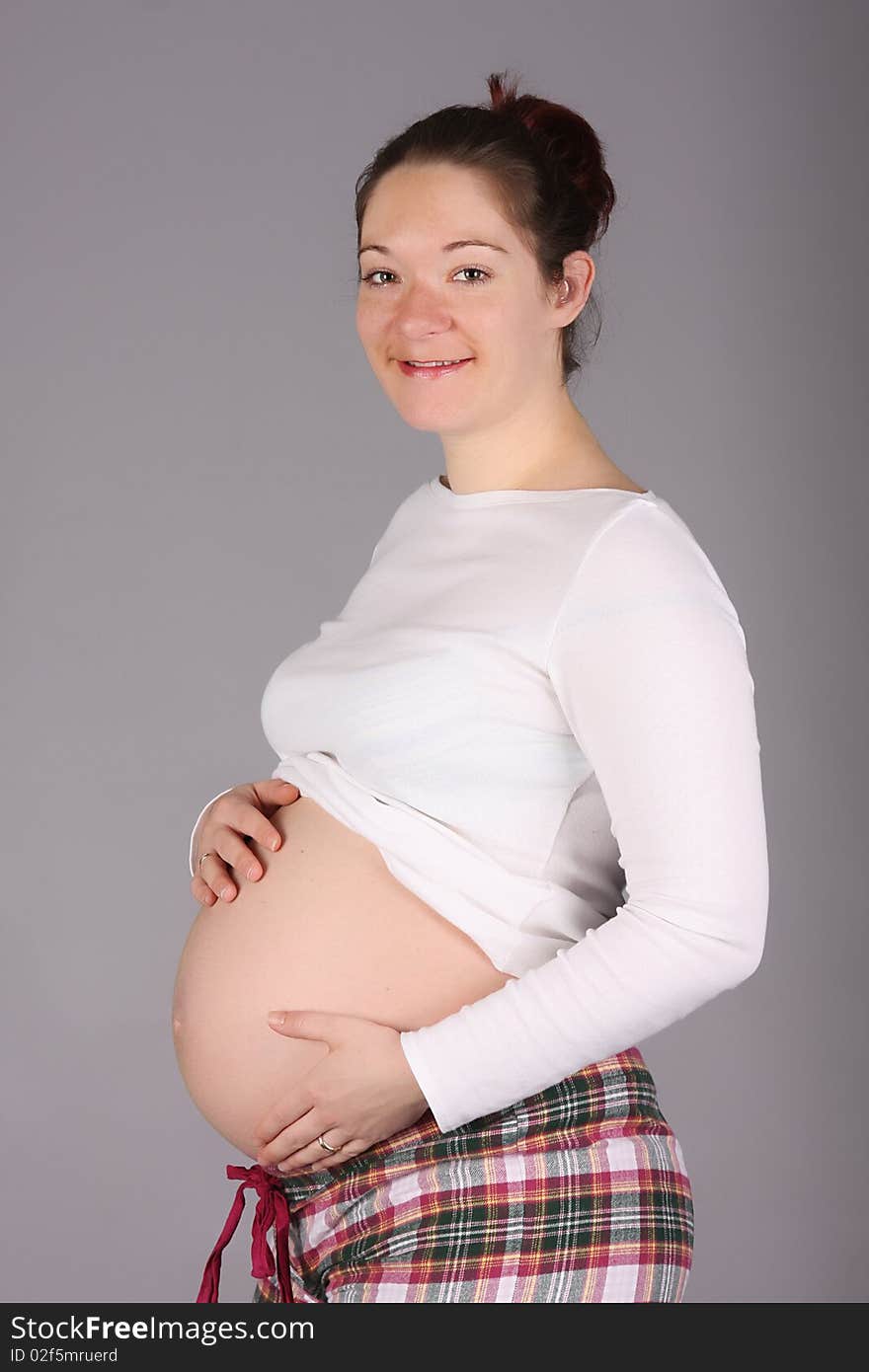 Pregnant woman holding belly on grey background