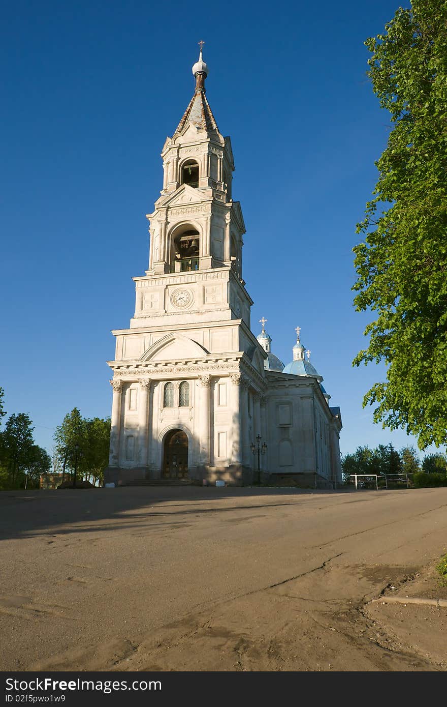 High bell tower of white church on evening light