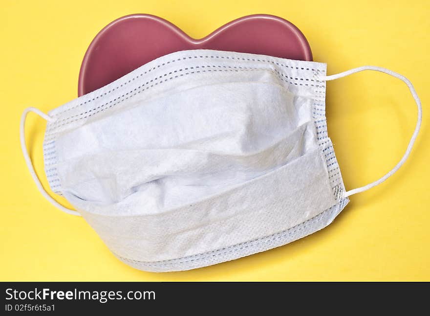 Surgical Mask over a Heart on a Yellow Background.  Good image for heart health or surgery. Surgical Mask over a Heart on a Yellow Background.  Good image for heart health or surgery.