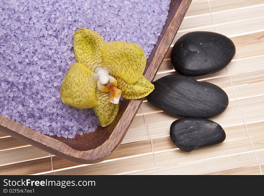 Spa scene with orchids, bath salts and massage stones on a bamboo mat.