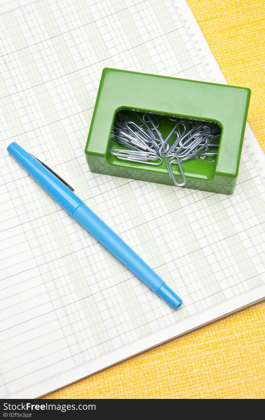 Paperclips, and a pen sit on a ruled page on a yellow background for the modern office worker. Paperclips, and a pen sit on a ruled page on a yellow background for the modern office worker.