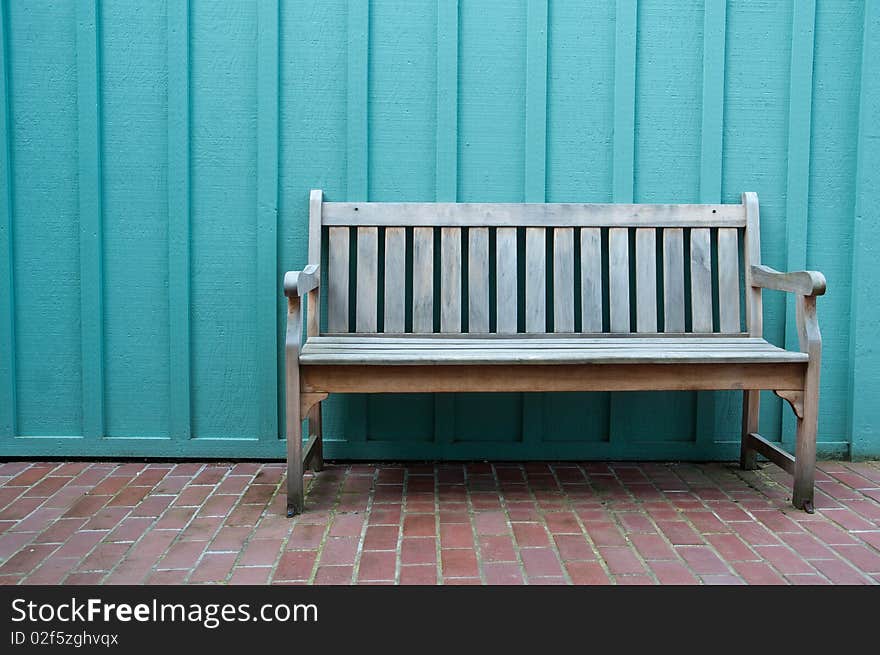 A weathered wood bench sits on bricks against blue wall