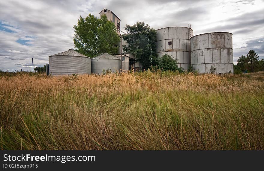 Wind blown grass with rusty silos against cloudy background. Wind blown grass with rusty silos against cloudy background