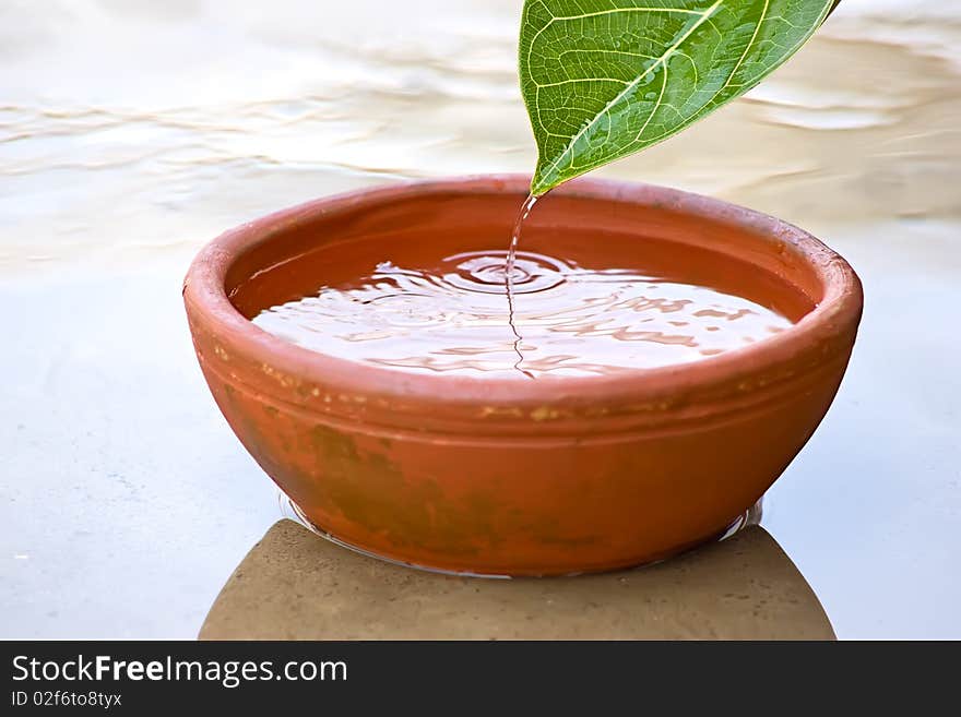 Dropping Water drops from green leaf into red clay bowl. Dropping Water drops from green leaf into red clay bowl