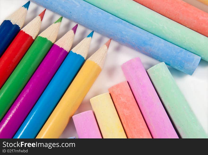 Close up capturing a selection of coloured chalks and pencils arranged over white. Close up capturing a selection of coloured chalks and pencils arranged over white.