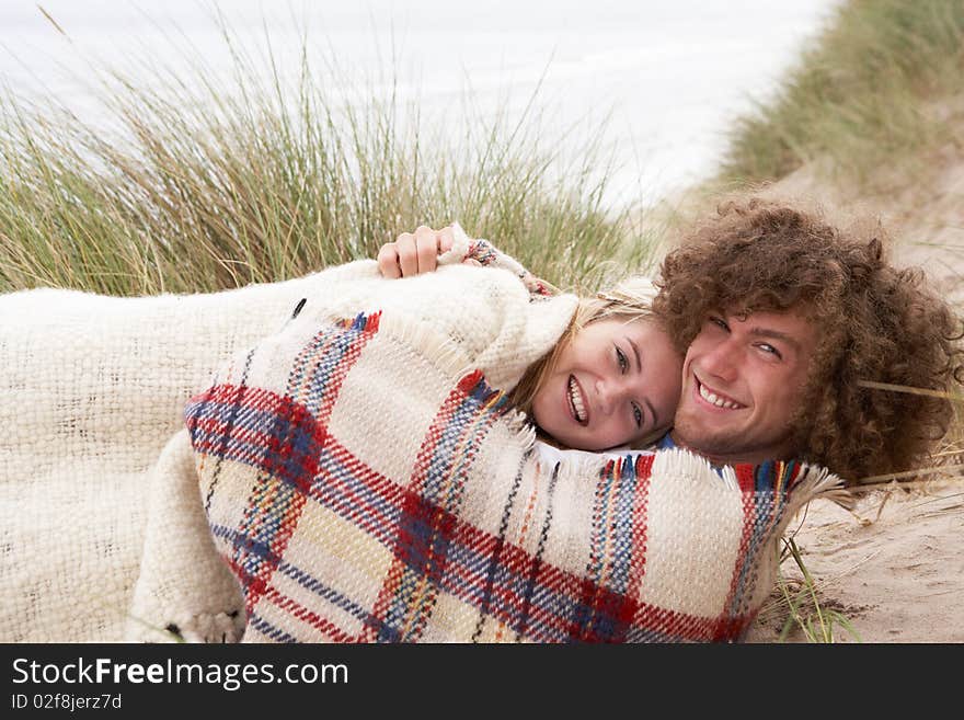 Teenage Couple Sitting In Sand Dunes Wrapped In Blanket