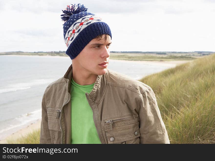 Teenage Boy Standing In Sand Dunes Wearing Woolly Hat