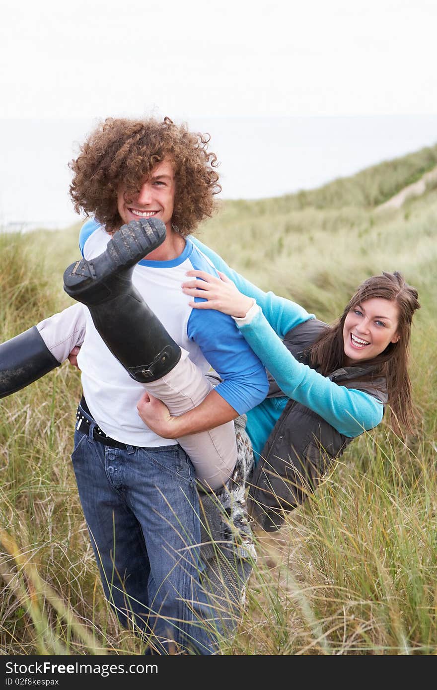 Teenage Couple Having Piggy Back Ride In Sand Dunes