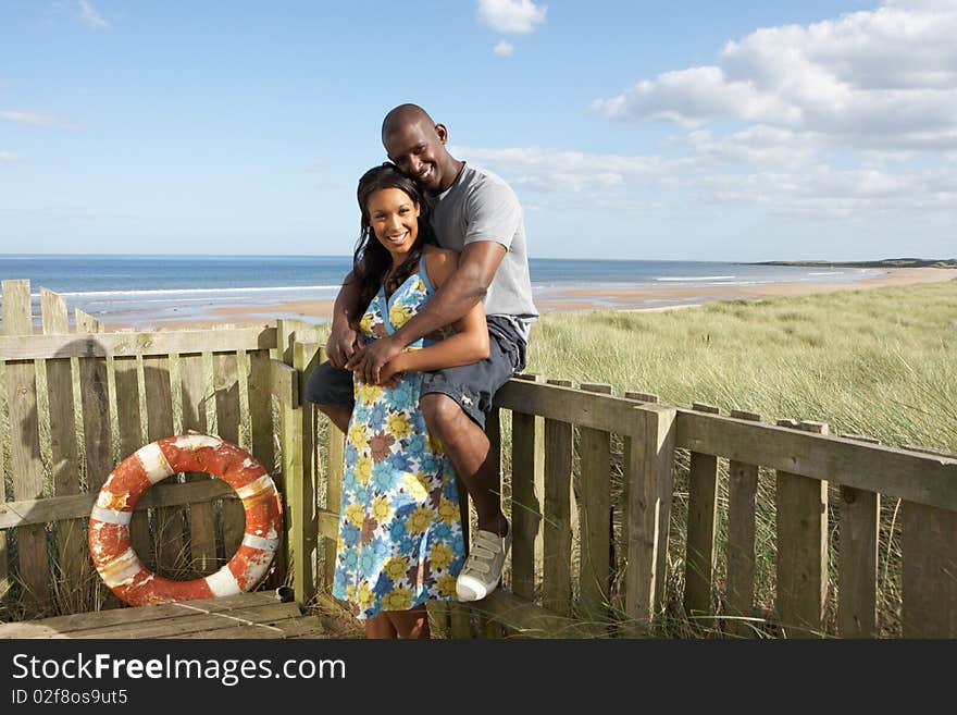 Romantic Young Couple Standing By Wooden Fence Of Beach Hut Amongst Dunes