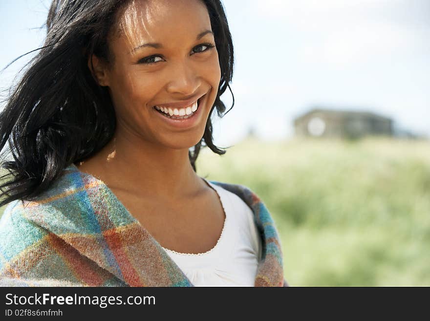 Smiing Young Woman Standing On Beach Wrapped In Blanket