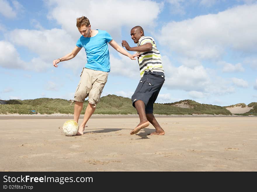 Two Young Men Palying Football On Beach Together