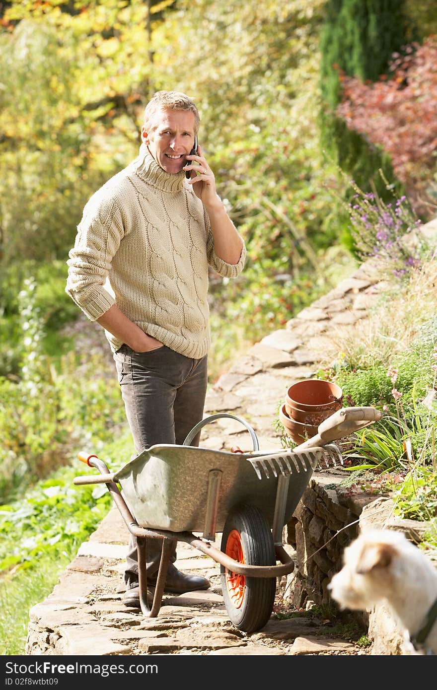 Man Outdoors On Mobile Phone With Dog Whilst On Break From Gardening