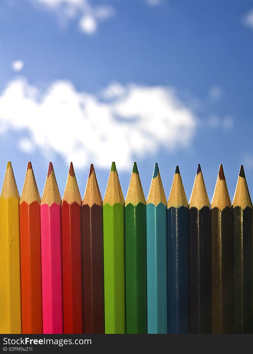 Colour pencils in a row, fence, background sky out of focus. Colour pencils in a row, fence, background sky out of focus