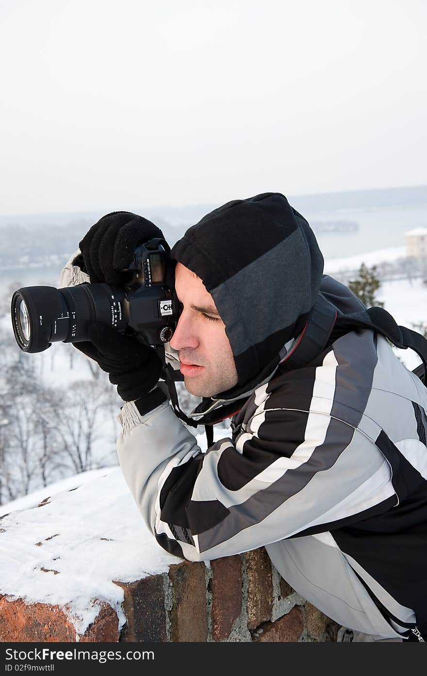 Young man, photographing in winter, focused and ready to shoot, leaning on a wall to stabilize his posture. Young man, photographing in winter, focused and ready to shoot, leaning on a wall to stabilize his posture