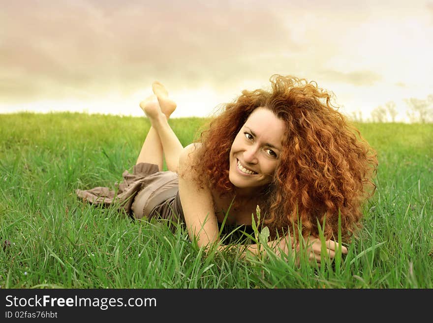 Smiling red haired woman lying on a green meadow. Smiling red haired woman lying on a green meadow