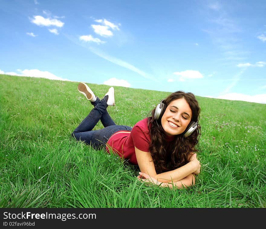 Smiling young woman lying on a green meadow and listening to music. Smiling young woman lying on a green meadow and listening to music