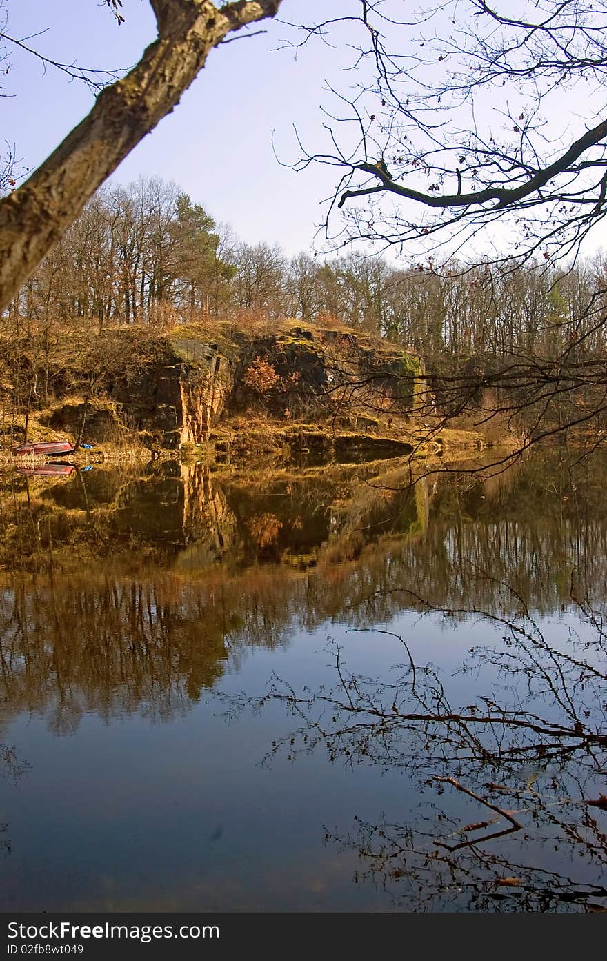 Cliff with trees and shrubs in the spring at a pond with reflections. Cliff with trees and shrubs in the spring at a pond with reflections.