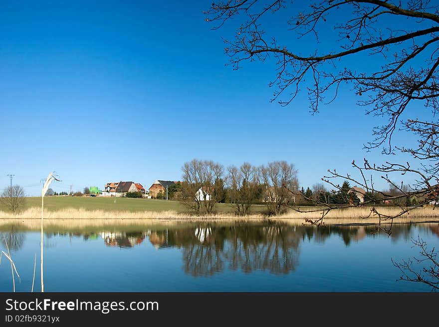 Small village at the lake bank in the spring sun with reflection on the water surface.