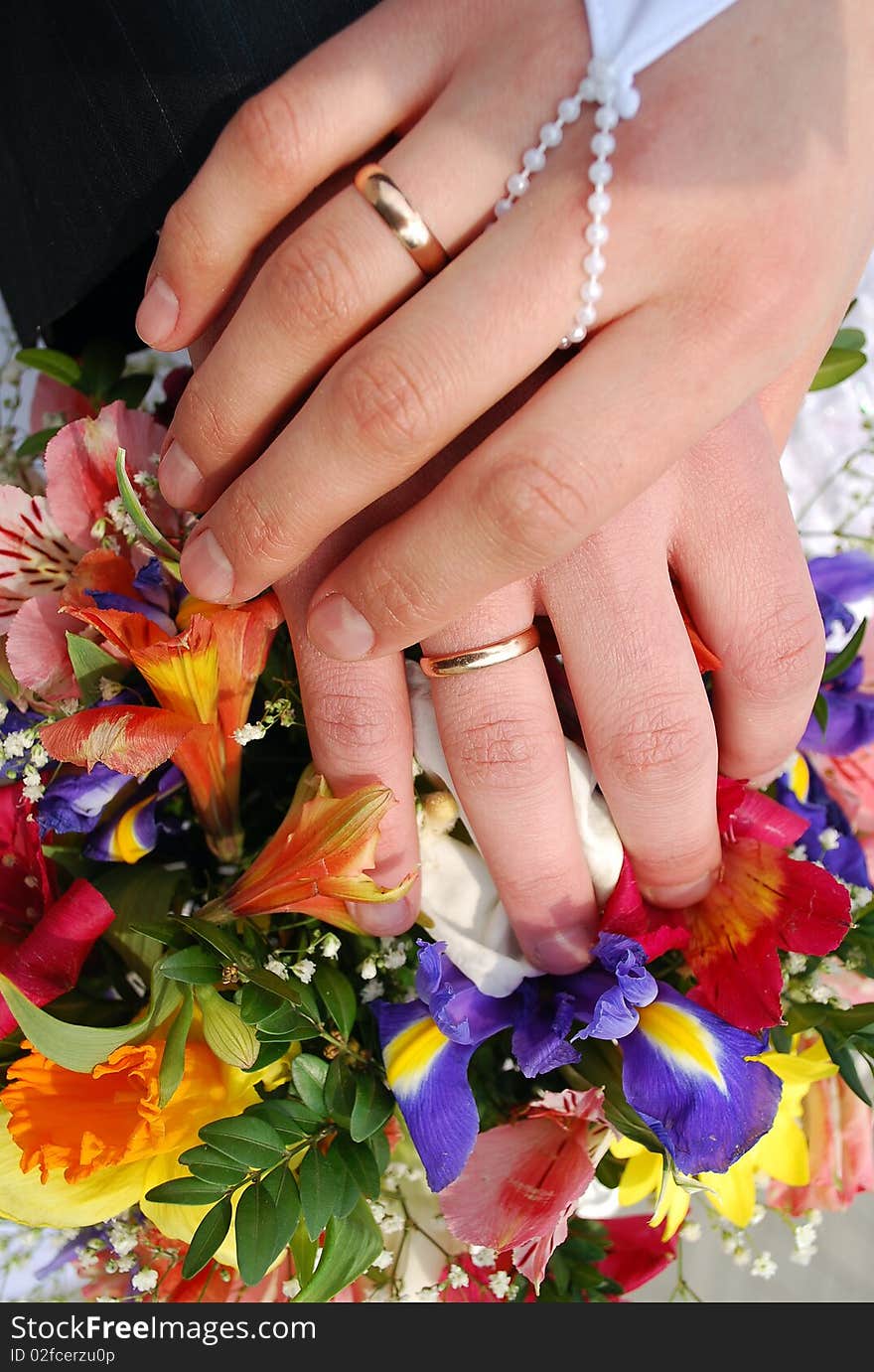 Hands of the groom and the bride with wedding rings on top of the bride's bouquet