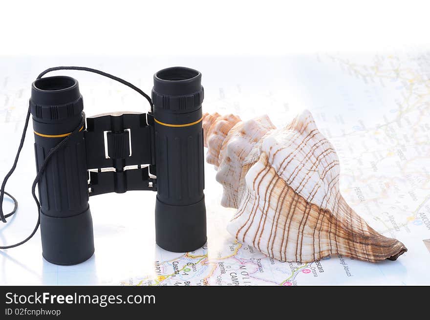Concept of travel to see, black binoculars and a big sea shell on a map. Concept of travel to see, black binoculars and a big sea shell on a map