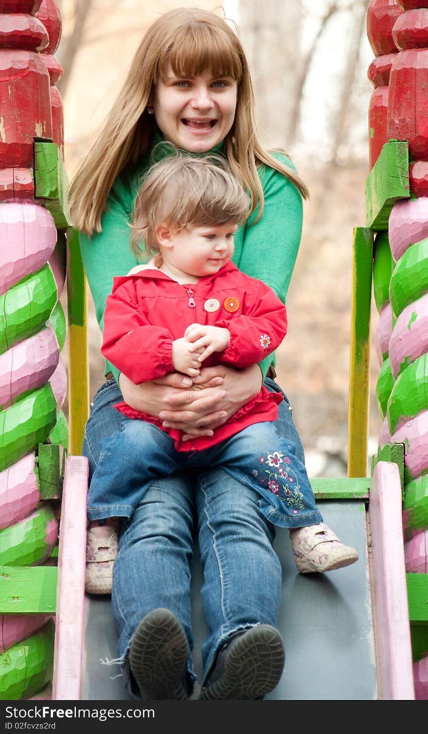 A young woman sitting at the top of a slide with a little girl on her knees at a playground. A young woman sitting at the top of a slide with a little girl on her knees at a playground