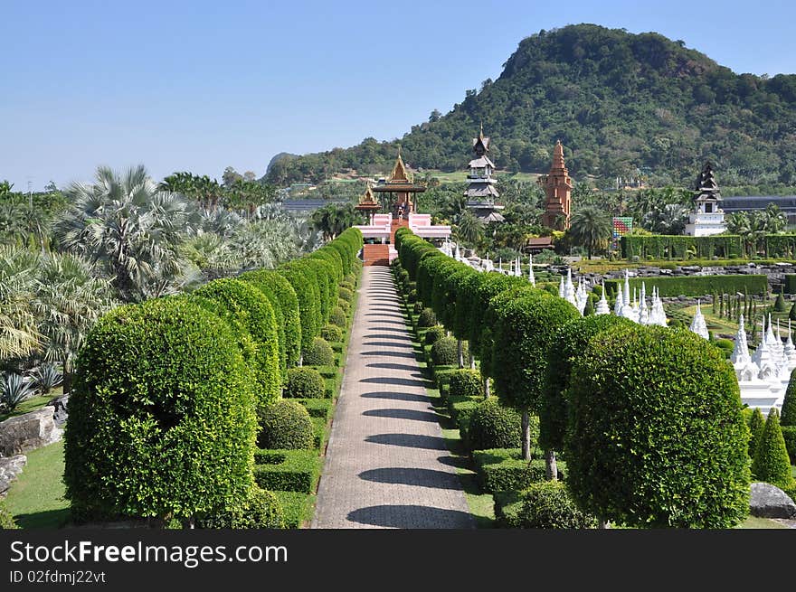 Clipped bushes line a pathway leading to one of the Thai viewing pavilions overlooking the formal French garden and its white Chedis and distant pagoda towers at Nong Nooch Tropical Gardens in Pattaya, Thailand. Clipped bushes line a pathway leading to one of the Thai viewing pavilions overlooking the formal French garden and its white Chedis and distant pagoda towers at Nong Nooch Tropical Gardens in Pattaya, Thailand.