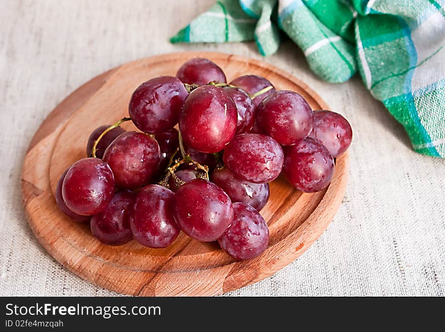 Red grapes on wooden plate on fabric background with kitchen towel