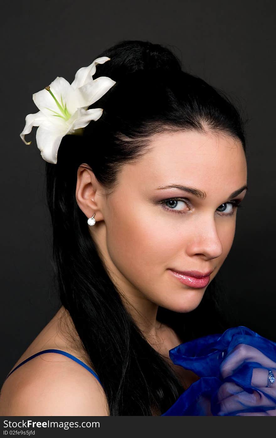 Beautiful woman with a white lily in dark hair, a portrait on a black background.