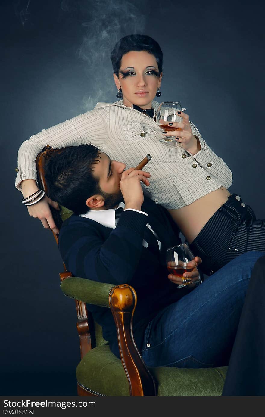 There is cool couple. He smokes cigar and hold glass with cognac. There is cool couple. He smokes cigar and hold glass with cognac.